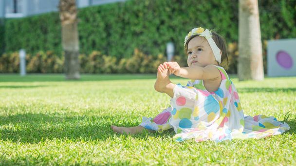 Little girl in colorful dress sitting on the grass - Photo, image