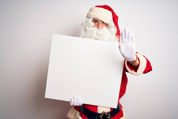 Orta yaşlı bir adam Noel Baba kostümü giyiyor. Beyaz arka planda afiş taşıyor. Açık elle dur işareti yapıyor. - Fotoğraf, Görsel