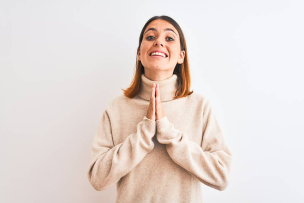 Beautiful redhead woman wearing winter turtleneck sweater over isolated background praying with hands together asking for forgiveness smiling confident. - Photo, Image