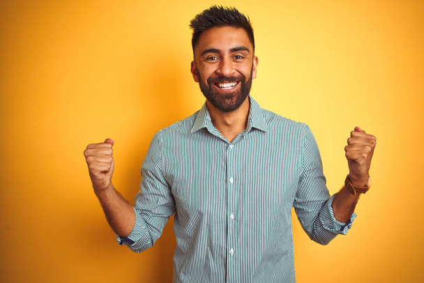 Fiatal indiai férfi zöld csíkos ing áll az elszigetelt sárga háttér ünneplő meglepett és csodálkozott a siker karokkal felemelt és nyitott szemmel. Nyertes koncepció. - Fotó, kép
