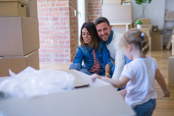Mooie familie, ouders en klein meisje in nieuw huis rond kartonnen dozen - Foto, afbeelding