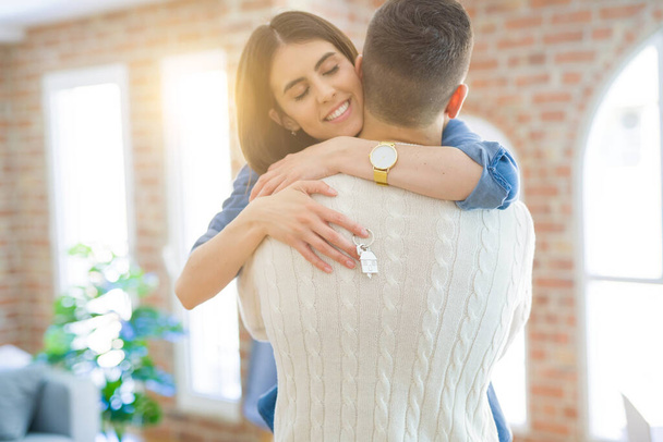 junges Paar zieht in ein neues Zuhause, umarmt sich verliebt und zeigt Schlüssel  - Foto, Bild