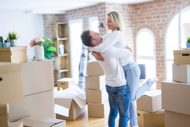 Schönes junges Paar umarmt sich im neuen Zuhause um Kartons - Foto, Bild
