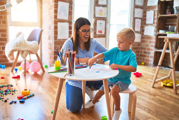Mladé bělošské dítě hrající si s učitelkou na škole. Matka a syn v herně kreslit remízu s barevnými tužkami - Fotografie, Obrázek