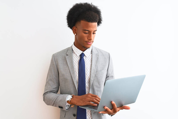 Giovane uomo d'affari afroamericano utilizzando computer portatile in piedi su sfondo bianco isolato con un'espressione fiduciosa sul viso intelligente pensando serio
 - Foto, immagini