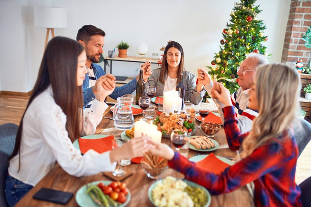 Bonita reunião familiar sorrindo feliz e confiante. Orar tomando as mãos antes de comer peru assado celebrando o Natal em casa
 - Foto, Imagem