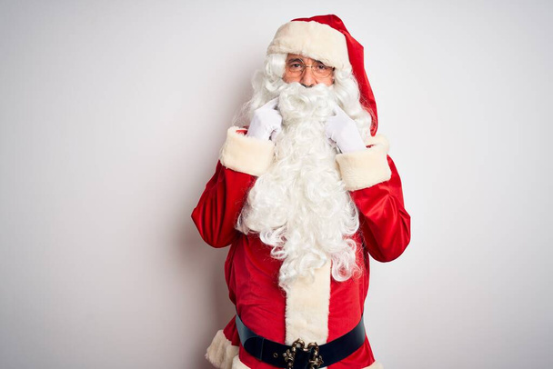 gutaussehender Mann mittleren Alters im Weihnachtsmannkostüm, der vor isoliertem weißem Hintergrund steht und mit offenem Mund lächelt, die Finger zeigt und ein fröhliches Lächeln erzwingt - Foto, Bild