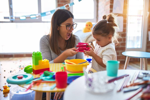 Jovem e bela professora e criança brincando com alimentos de plástico e brinquedos de talheres no jardim de infância
 - Foto, Imagem