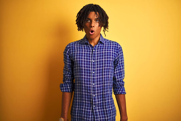 Afro man with dreadlocks wearing casual shirt standing over isolated yellow background afraid and shocked with surprise expression, fear and excited face. - Photo, Image