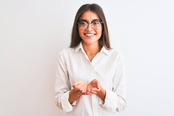 Young beautiful businesswoman wearing glasses standing over isolated white background Smiling with hands palms together receiving or giving gesture. Hold and protection - 写真・画像