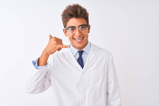 若いハンサムな科学者の男性が眼鏡をかけてコートを着て、電話で話すような手と指で電話のジェスチャーをして笑顔で孤立した白い背景の上に。概念の伝達. - 写真・画像