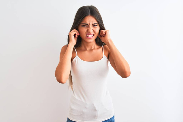 Jeune belle femme portant un t-shirt décontracté debout sur fond blanc isolé couvrant les oreilles avec des doigts avec une expression agacée pour le bruit de la musique forte. Concept sourd
. - Photo, image