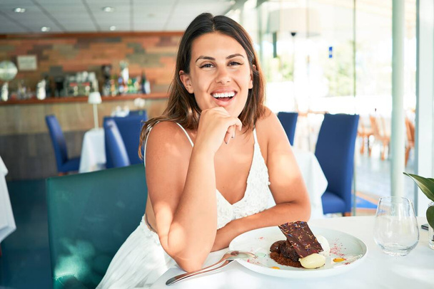 Young beautiful woman sitting at restaurant enjoying summer vacation eating delicious chocolate dessert - Foto, Imagem