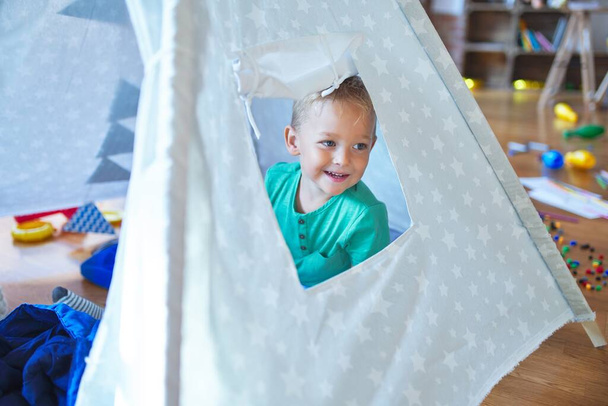 愛らしい金髪の幼児は、テープの中で幸せに笑っています。幼稚園のおもちゃの周りで遊んでいる床に座って - 写真・画像