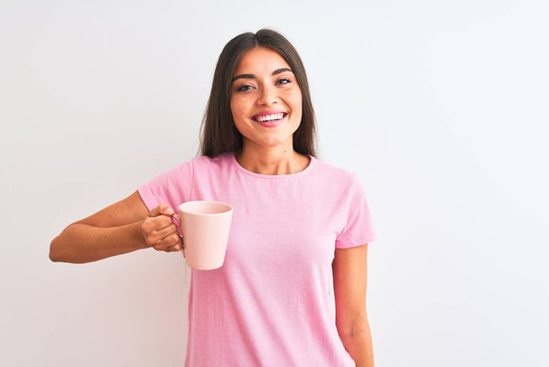 Young beautiful woman drinking pink cup of coffee standing over isolated white background with a happy face standing and smiling with a confident smile showing teeth - Фото, изображение