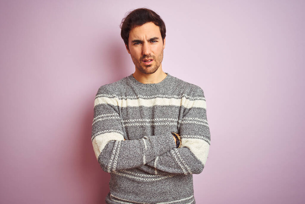 Young handsome man wearing casual striped sweater standing over isolated pink background skeptic and nervous, disapproving expression on face with crossed arms. Negative person. - Fotó, kép