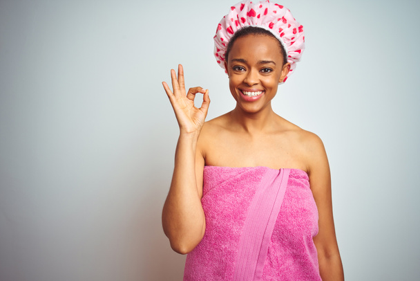 African american woman wearing pink shower towel after bath over isolated background smiling positive doing ok sign with hand and fingers. Successful expression. - Photo, Image