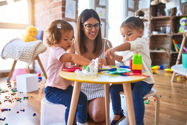 Jeune belle enseignante et tout-petits jouant des repas en utilisant de la nourriture en plastique et des couverts jouet à la maternelle
 - Photo, image