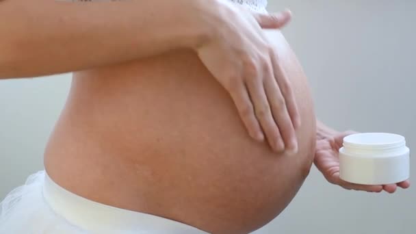 Κοντινό πλάνο ενός έγκυου κοριτσιού τρίβει ραγάδες κρέμα στο δέρμα του στομάχου της - Πλάνα, βίντεο