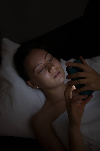 mujer joven acostada en la cama y usando un teléfono inteligente
 - Foto, imagen