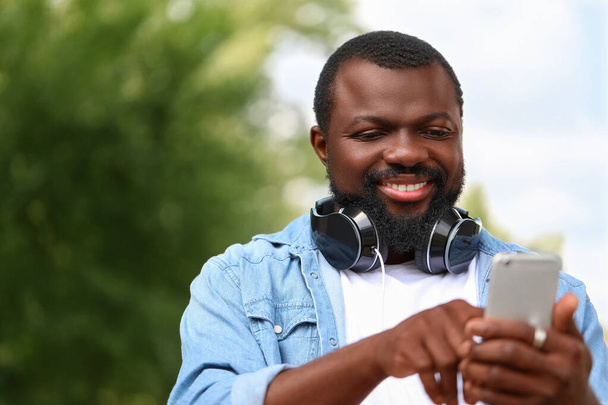 携帯電話とヘッドフォンを屋外に持つハンサムなアフリカ系アメリカ人男性 - 写真・画像