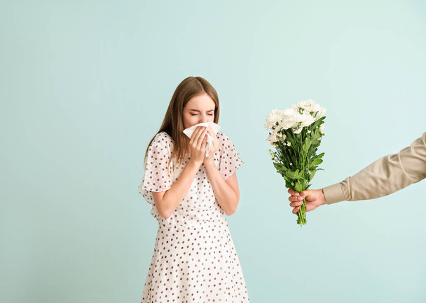 Man giving flowers to young woman suffering from allergy on light background - Photo, Image