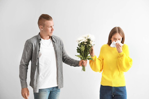 Uomo dando fiori alla giovane donna che soffre di allergia su sfondo chiaro
 - Foto, immagini