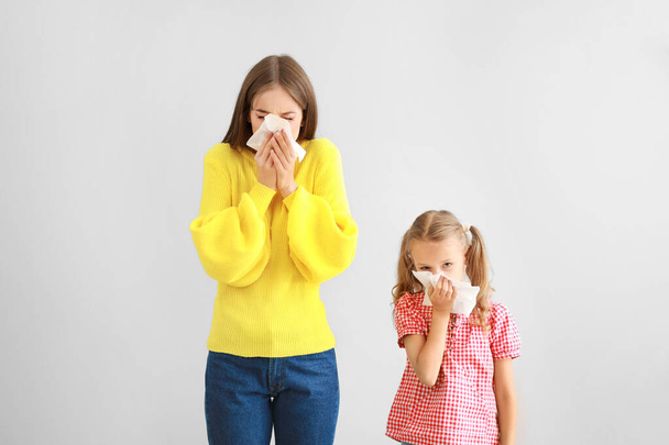 Mujer joven y niña que sufre de alergia en un fondo claro
 - Foto, Imagen