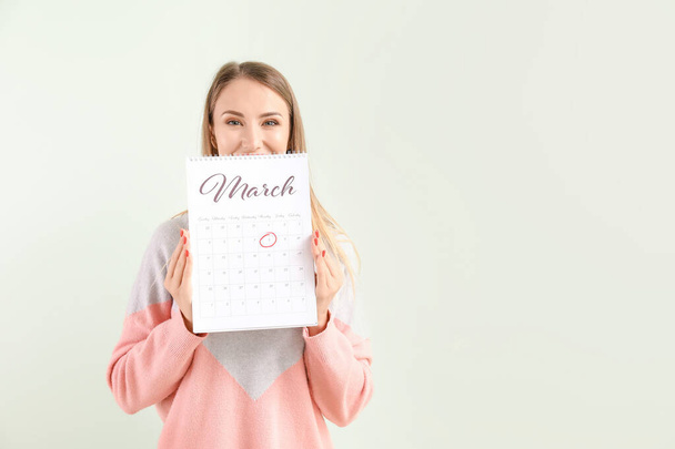 Krásná mladá žena s kalendářem na světlém pozadí. Mezinárodní oslava Dne žen - Fotografie, Obrázek
