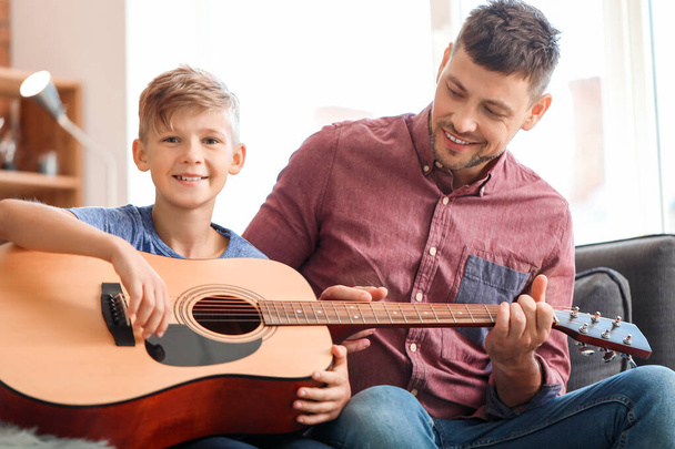 Ο πατέρας που διδάσκουν το μικρό του γιο να παίζουν κιθάρα στο σπίτι - Φωτογραφία, εικόνα