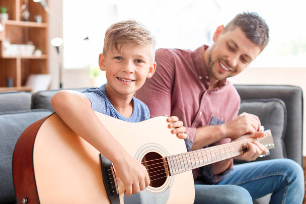 Padre enseñando a su hijito a tocar la guitarra en casa
 - Foto, imagen