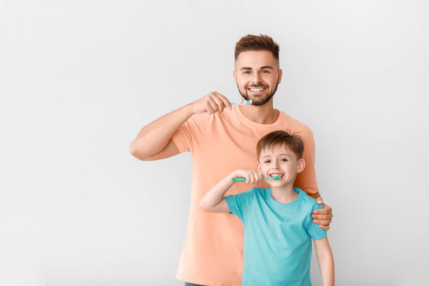Portrait of man and his little son brushing teeth on light background - Photo, Image