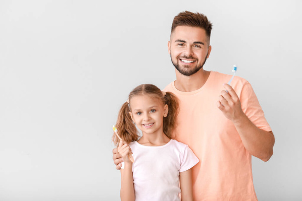Portrait of man and his little daughter brushing teeth on light background - Fotoğraf, Görsel