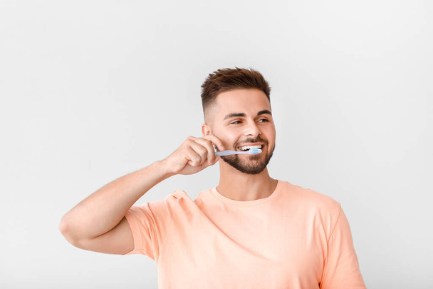 Portrait of man brushing teeth on light background - Фото, изображение