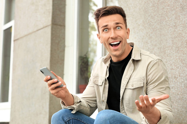 Удивленный молодой человек с мобильным телефоном на улице
 - Фото, изображение