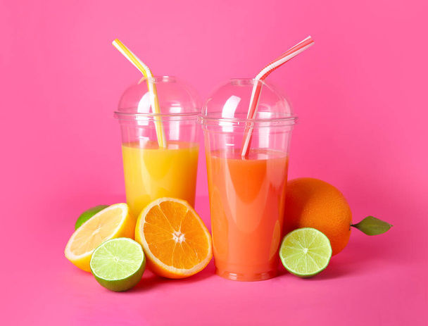 Plastic cups of fresh juices with citrus fruits on color background - Photo, Image