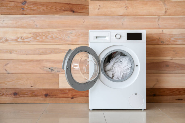 Lavadora moderna con lavadero cerca de pared de madera
 - Foto, imagen