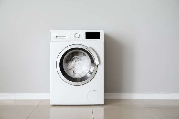 moderne Waschmaschine mit Wäsche in der Nähe der weißen Wand - Foto, Bild