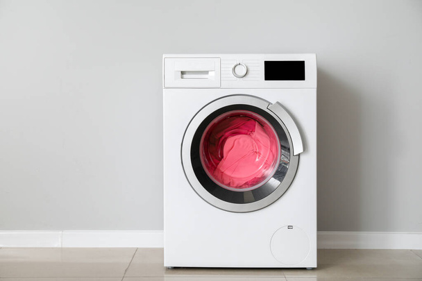 Máquina de lavar roupa moderna com lavanderia perto da parede branca
 - Foto, Imagem
