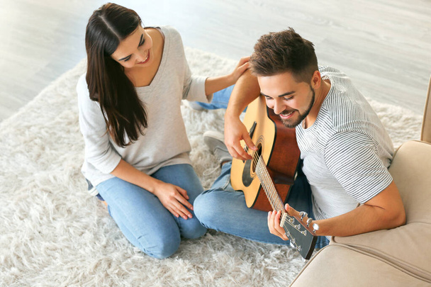 Evde gitar çalan güzel genç bir çift. - Fotoğraf, Görsel