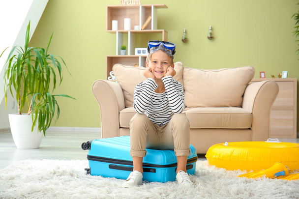 Cute little boy sitting on suitcase at home - Fotoğraf, Görsel