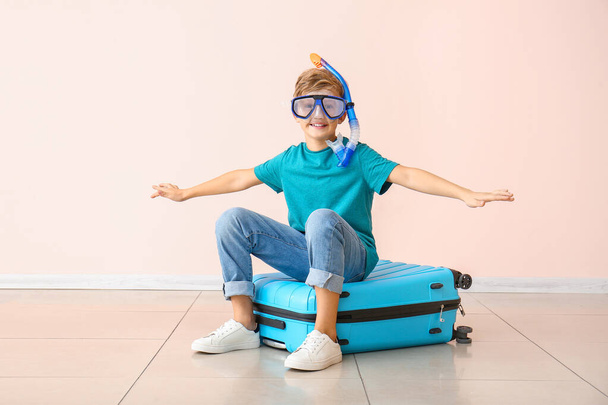 Cute little boy with snorkeling mask sitting on suitcase near color wall - Фото, изображение