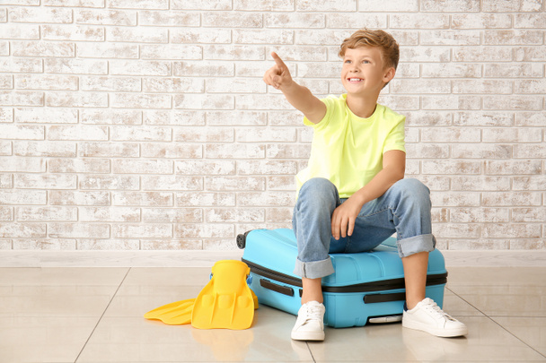 Cute little boy with suitcase pointing at something against brick wall - Photo, Image