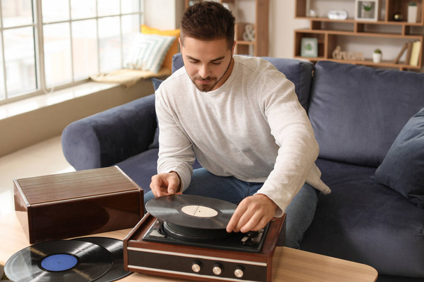 Young man listening to music through record player at home - Фото, изображение