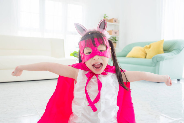 幸せな小さなアジアの女の子身に着けていますピンクスーパーヒーロー布ストレッチ彼女の腕  - 写真・画像