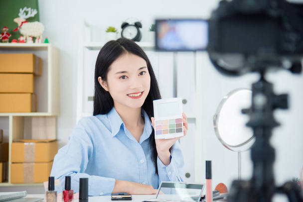 Красива азіатська дівчина тримає вітряну палітру, розповідаючи про свою повсякденну процедуру макіяжу перед камерою для запису відео у відеоблог
  - Фото, зображення