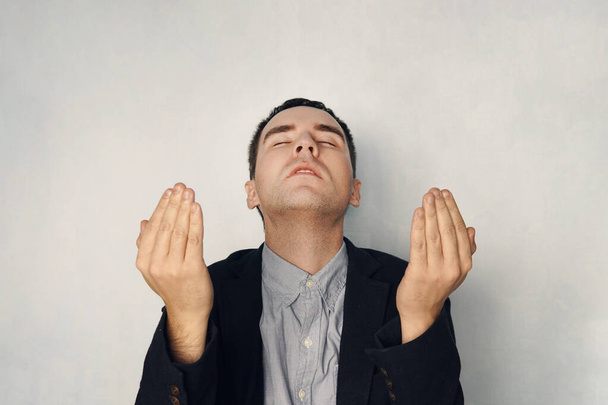 Um homem focado em um terno de negócios medita. homem de negócios levantou as mãos em oração. Uma petição pela bênção de Deus. Conceito de oração e meditação. fundo azul
 - Foto, Imagem