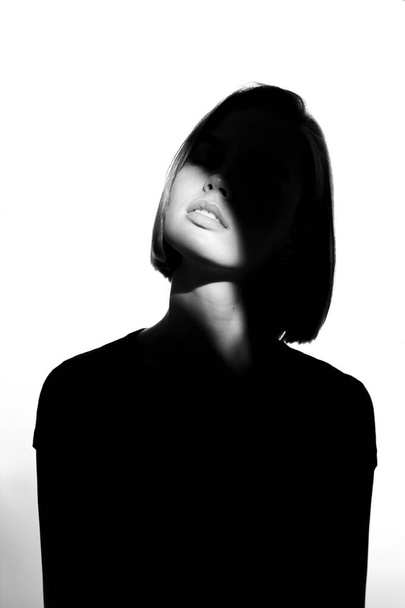 Fashionable beauty portrait. Black silhouette on white background. Girl with a spot of light on her face.  - 写真・画像