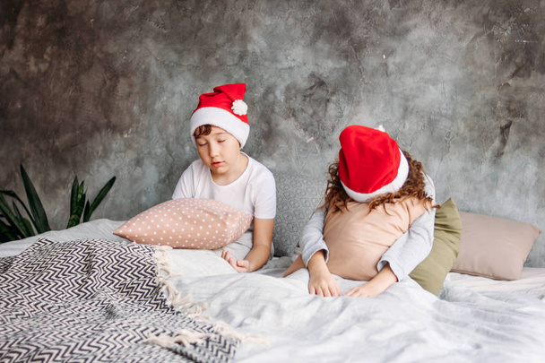 Cute tween children in Santa hats don't want to wake up on bed with pillow in loft bedroom, christmas morning time - 写真・画像