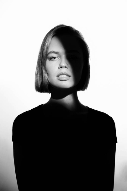Fashionable beauty portrait. Black silhouette on white background. Girl with a spot of light on her face.  - Foto, Bild